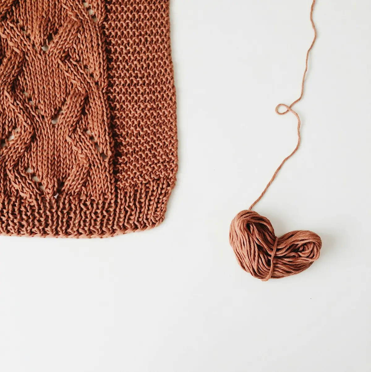 Rust-colored cable knit panel beside a heart shaped from yarn