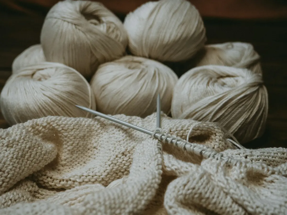 Cream yarn and knitting needles resting on a knitted throw